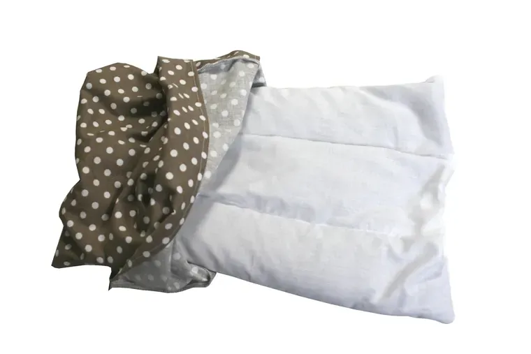 Coussin de tissu cloisonné sorti de sa housse à pois bruns, sur fond blanc
