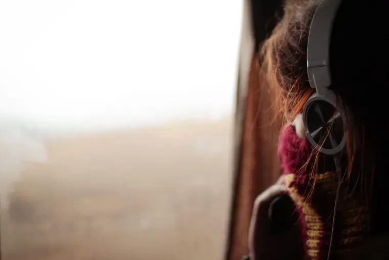 Personne de profil près d’une fenêtre, un casque audio sur les oreilles, le visage non visible