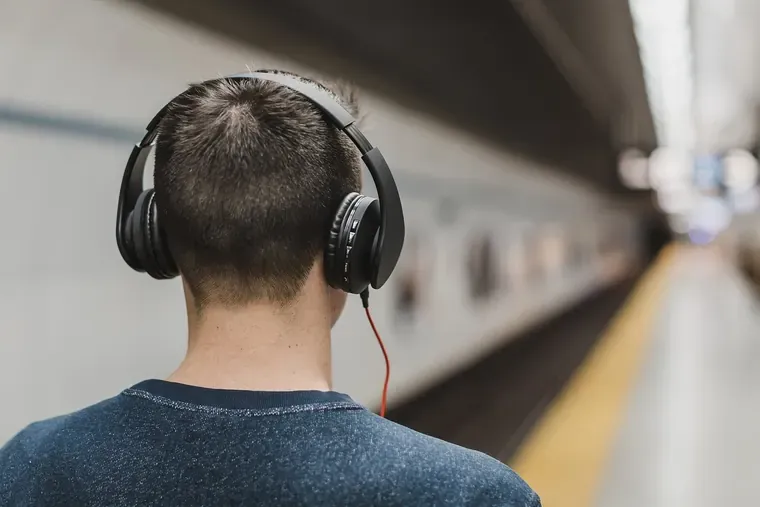 Homme vu de dos, un casque audio à arceau sur les oreilles, sur un quai de métro