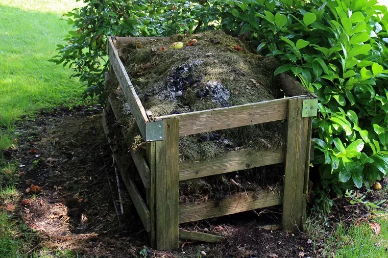 Composteur en bois rempli de déchets végétaux, dans un jardin