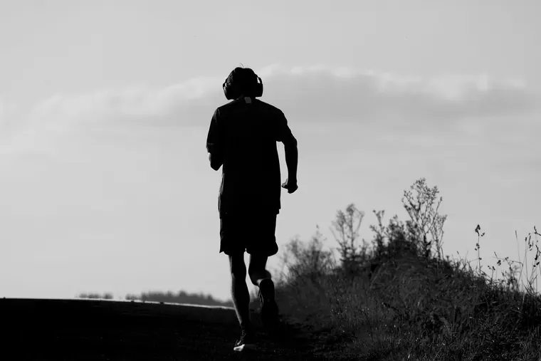 Silhouette d’un coureur vu de dos, un casque sur les oreilles, sur un chemin en contre-jour