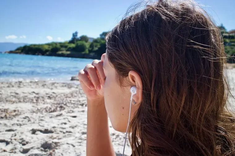 Jeune femme de profil sur une plage, un écouteur dans l’oreille et la main près du front