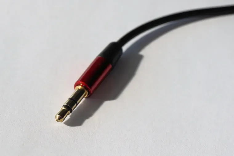 Fiche jack à embout rouge et doré au bout d’un câble noir, posée sur une surface claire