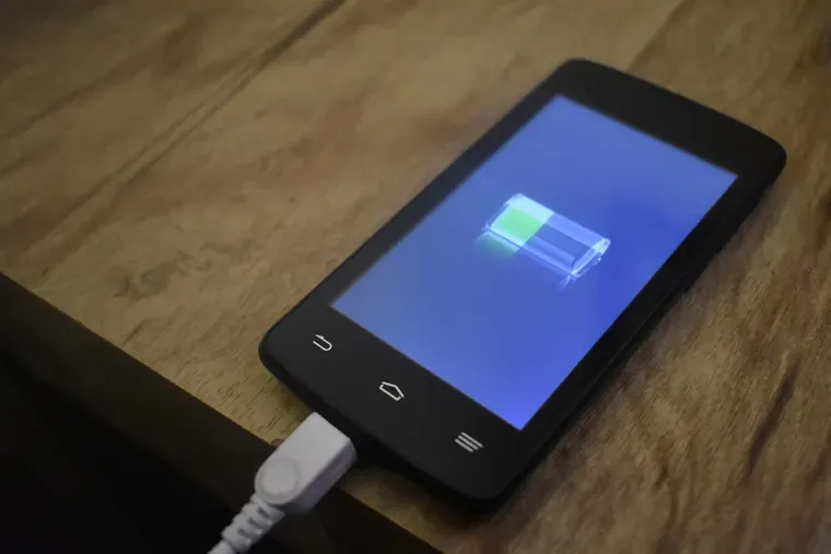 Téléphone mobile posé sur une table en bois, branché à un câble de charge, avec une icône de batterie à l’écran
